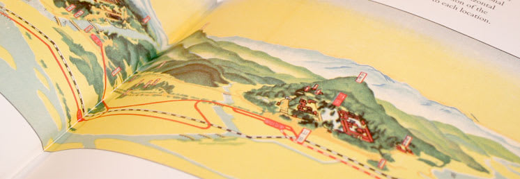 A photo of a colorful illustration of a map viewed at angle so that three-dimensional elements are depicted relative to the roads and railways that navigate the land.