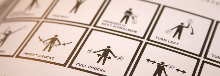 A photo of a bad illustration of the hand signals and motions for directing airplanes where the figures are purely black and white. It is visually difficult to distinguish the figures and their bodies from the positions and movements.