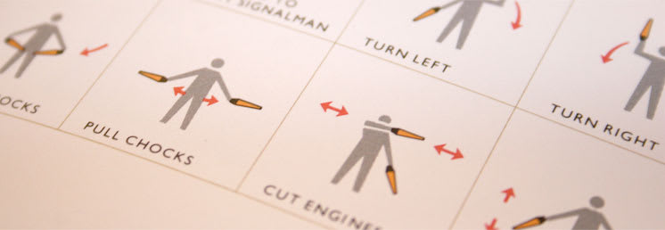 A photo of an improved illustration of the hand signals and motions for directing airplanes where the figures' body is lightened with the signals and movements using different colors to help make it easier to visually distinguish the elements.