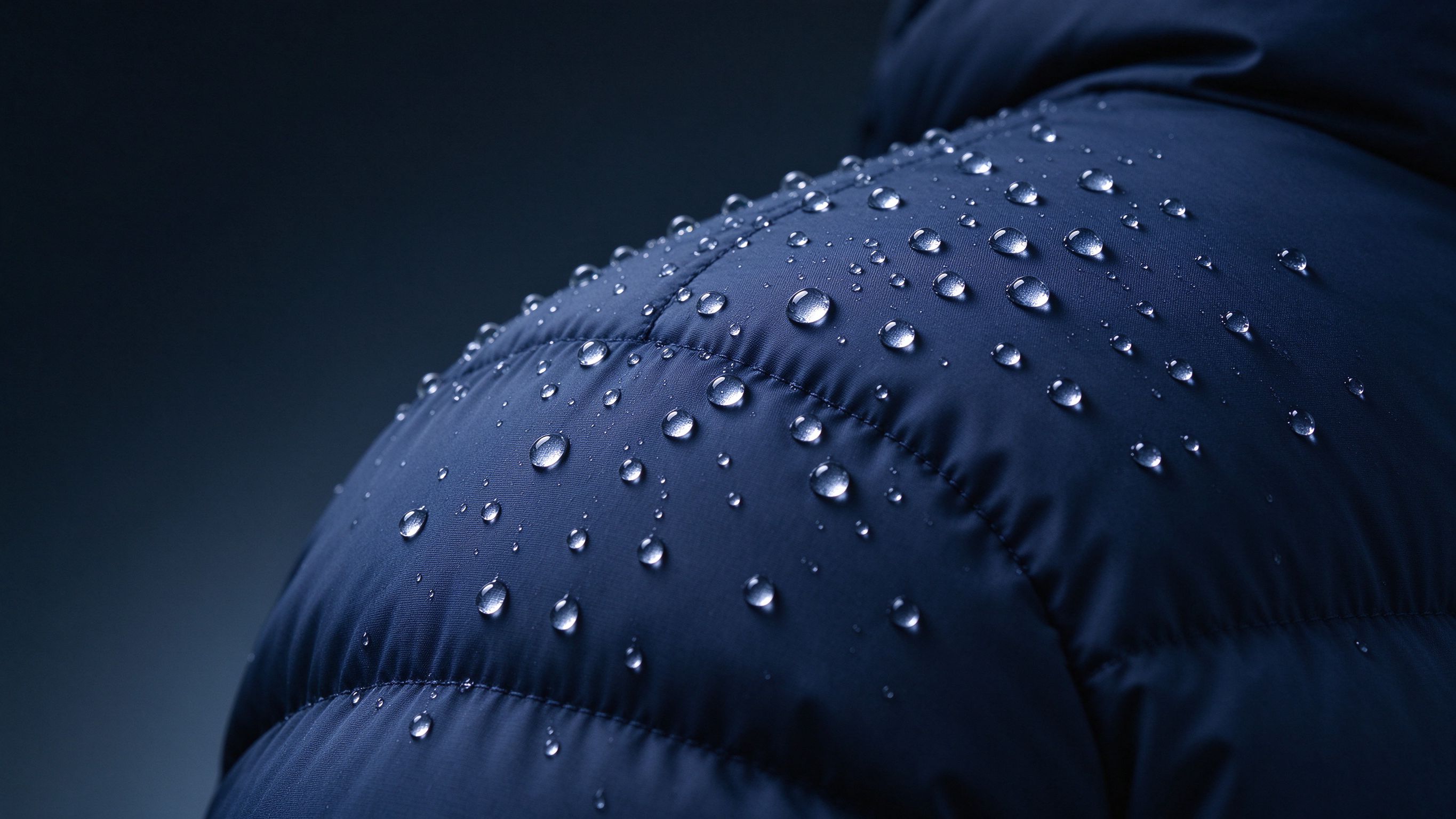 Water beads beading up on a deep blue puffer shell — durable water-repellent nylon