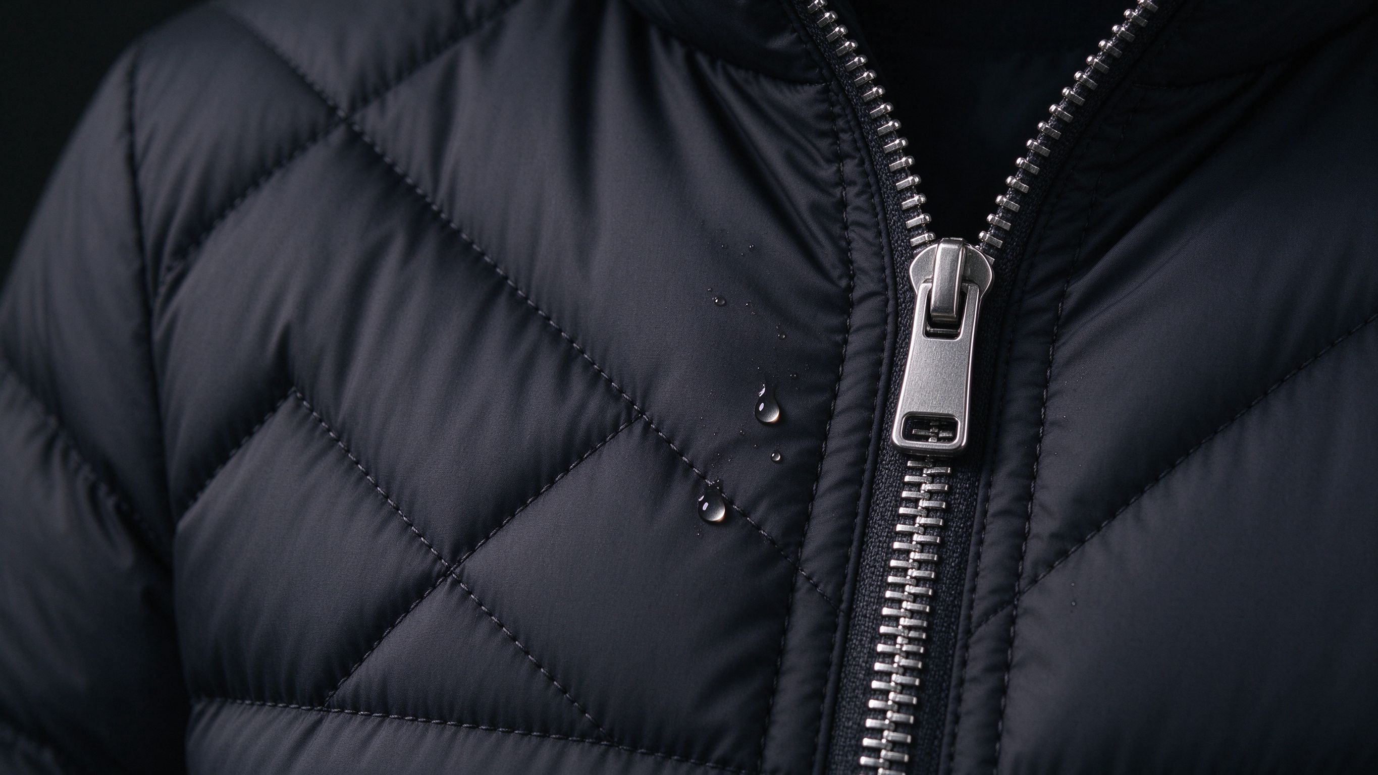 Quilted puffer fabric with a metal zipper and beading water droplets — technical shell details