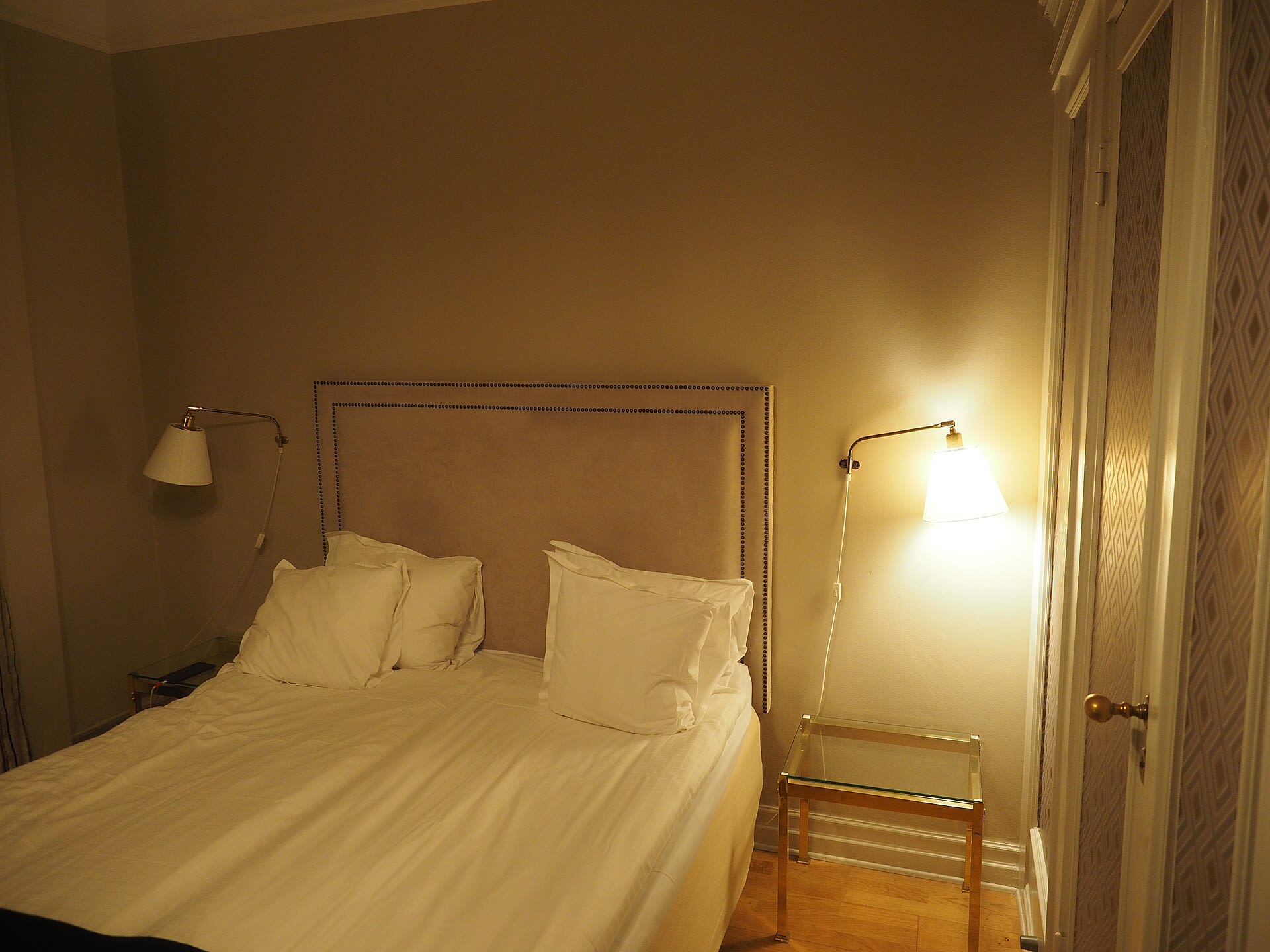 Hotel room with a made bed and lit bedside lamp