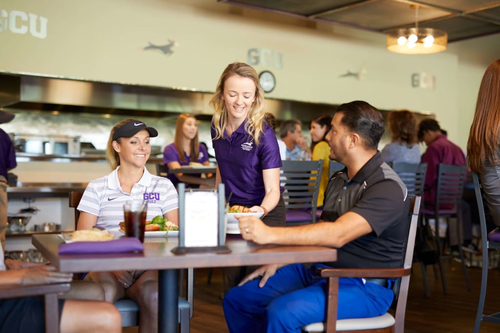 Golfers sitting at table with waitress serving them