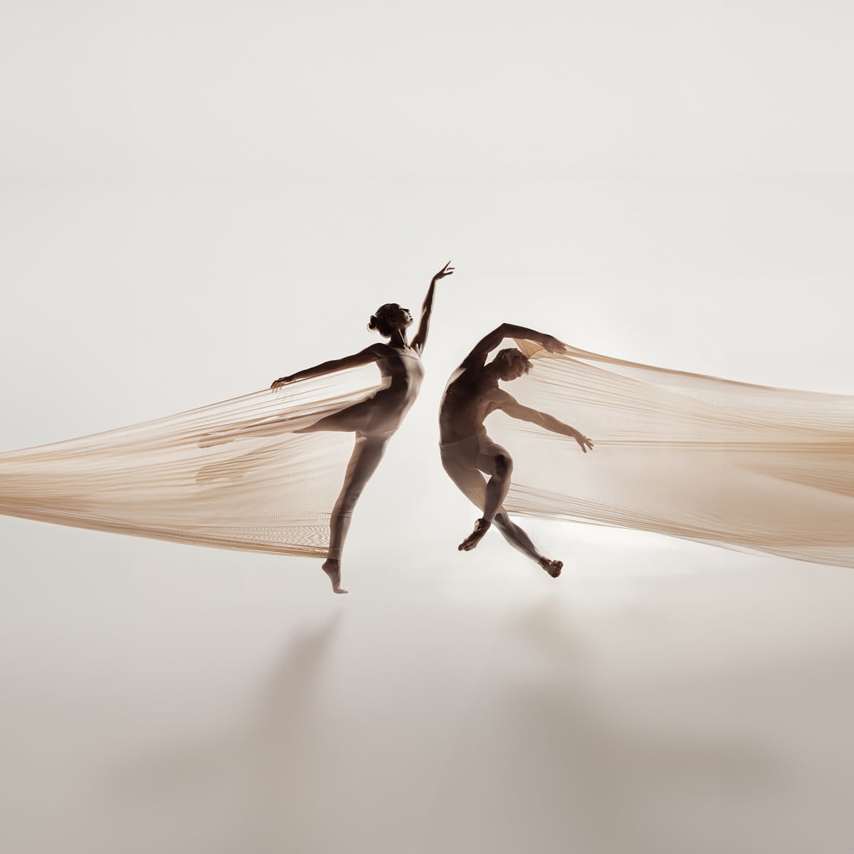 A male and a female dancer dancing with flowing tulle fabric in a bright studio