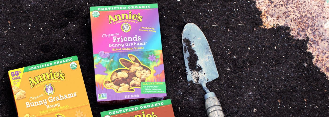 Boxes of Annie's crackers lying next to a hand spade in a pile of dark, fertile soil.