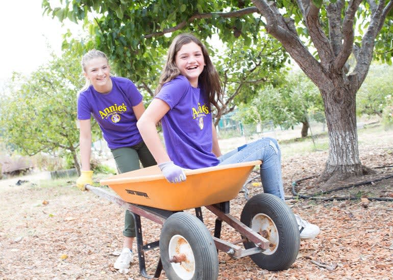 Two pre-teen girls laughing, while one pushes the other in a wheelbarrow