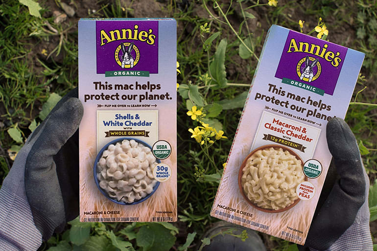 Hands wearing garden gloves holding two boxes of Annie's mac and cheese