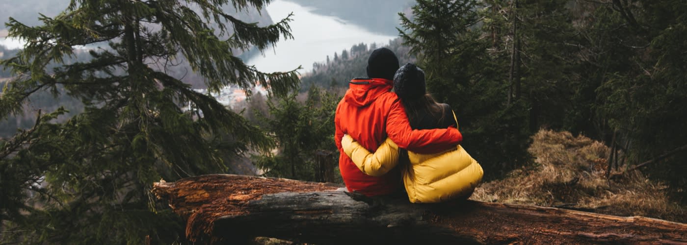 Couple sat on broken trunk of tree in forest enjoying landscape view