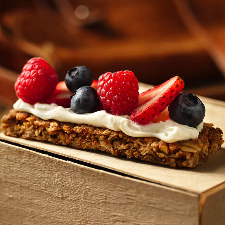 A Nature Valley Oats 'N Honey Crunchy Granola Bar spread with cream cheese and topped with fresh berries.