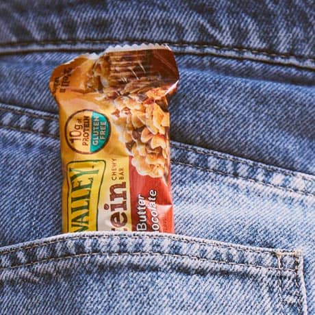 A Gluten-free Nature Valley granola bar sticking out of a pocket in a pair of denim jeans.