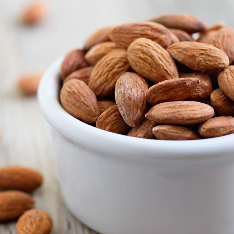 A white ramekin filled with whole almonds.