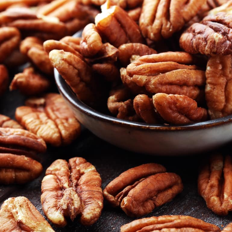 Whole pecans overflowing from a bowl.