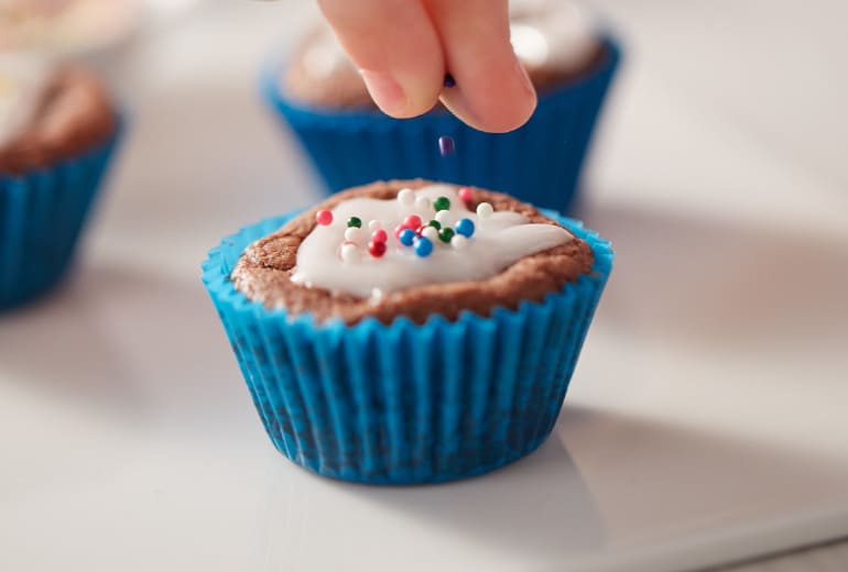 Close up on someone's hand sprinkling a brownie bite with sprinkles