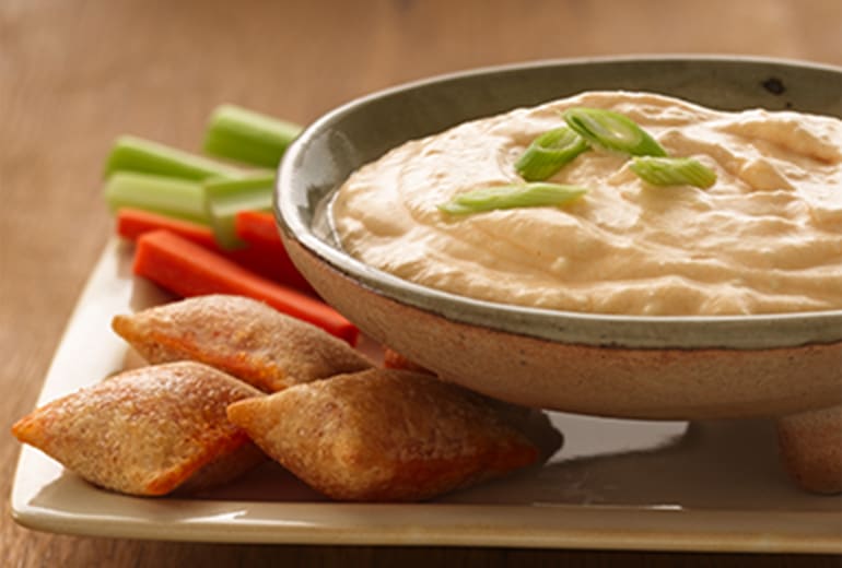 a bowl of buffalo cheese dip next to celery, carrots and Totino's pizza rolls