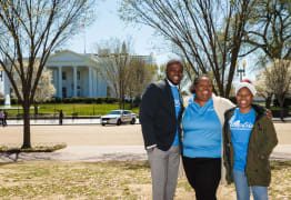 Wide shot of three people outside in a park on a sunny day smiling in Generation T shirts