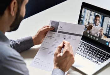 An image of a man reading a resume and interview a talent on through a video call on his laptop.