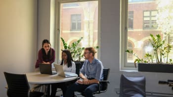 A diverse group of adult learners working together on laptops in a bright, modern training space at Generation Australia, with large windows and greenery in the background.