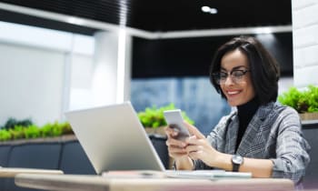 Business professional using a laptop and smartphone at a modern office desk