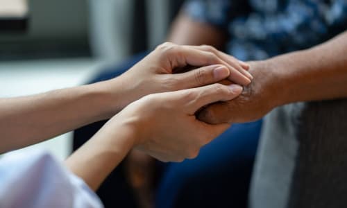 Care worker offering compassionate support by holding the hand of an older person