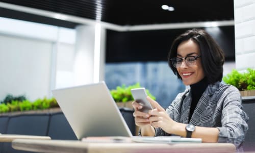 Business professional using a laptop and smartphone at a modern office desk