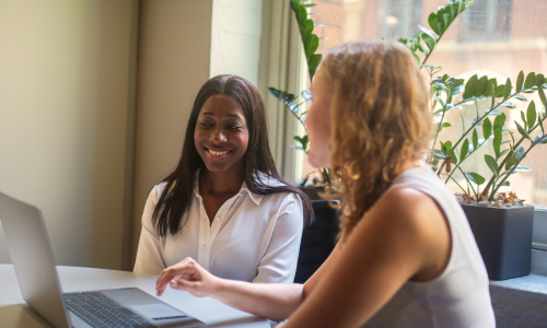 Two people smiling and talking while working on a laptop together