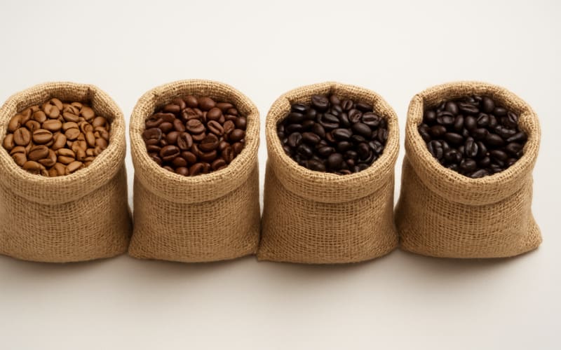A variety of coffee beans displayed in small burlap sacks, showing different shades of roast.