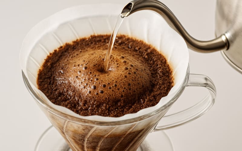 A close-up image of coffee grounds blooming as hot water is poured over them in a pour-over coffee maker.