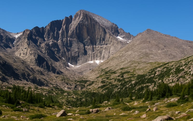 A panoramic view of Longs Peak with its rugged terrain and alpine scenery under a clear blue sky.