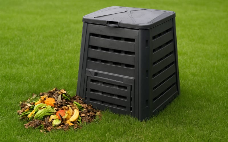 A compost bin with organic waste materials beside a lush green lawn.