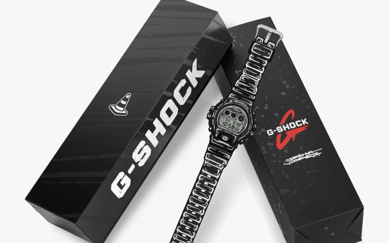 Black and white G-Shock digital watch with graphic strap and two black G-Shock branded boxes.