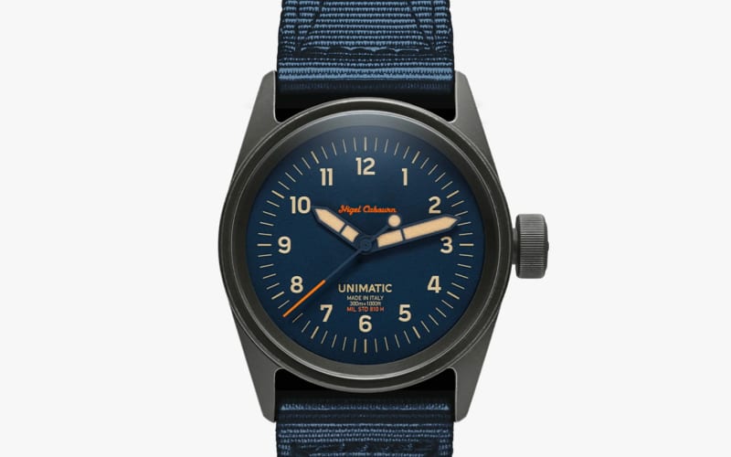 Black metal wristwatch with a blue dial, beige hands, orange second hand, and blue fabric strap.