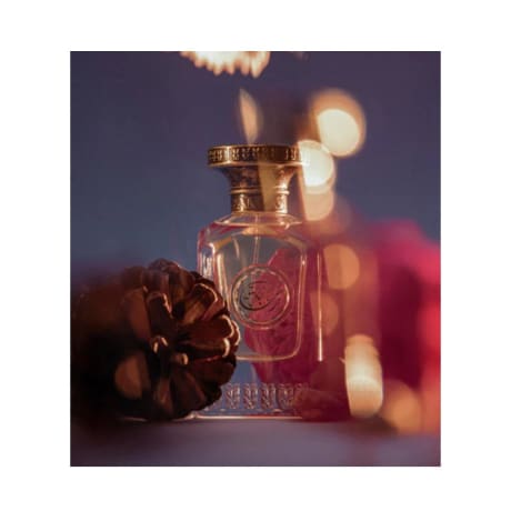 Flacon de parfum, Anfas (Rahaba Extrait), verre transparent avec détails dorés, bouchon cannelé, 80ml, pomme de pin à proximité.