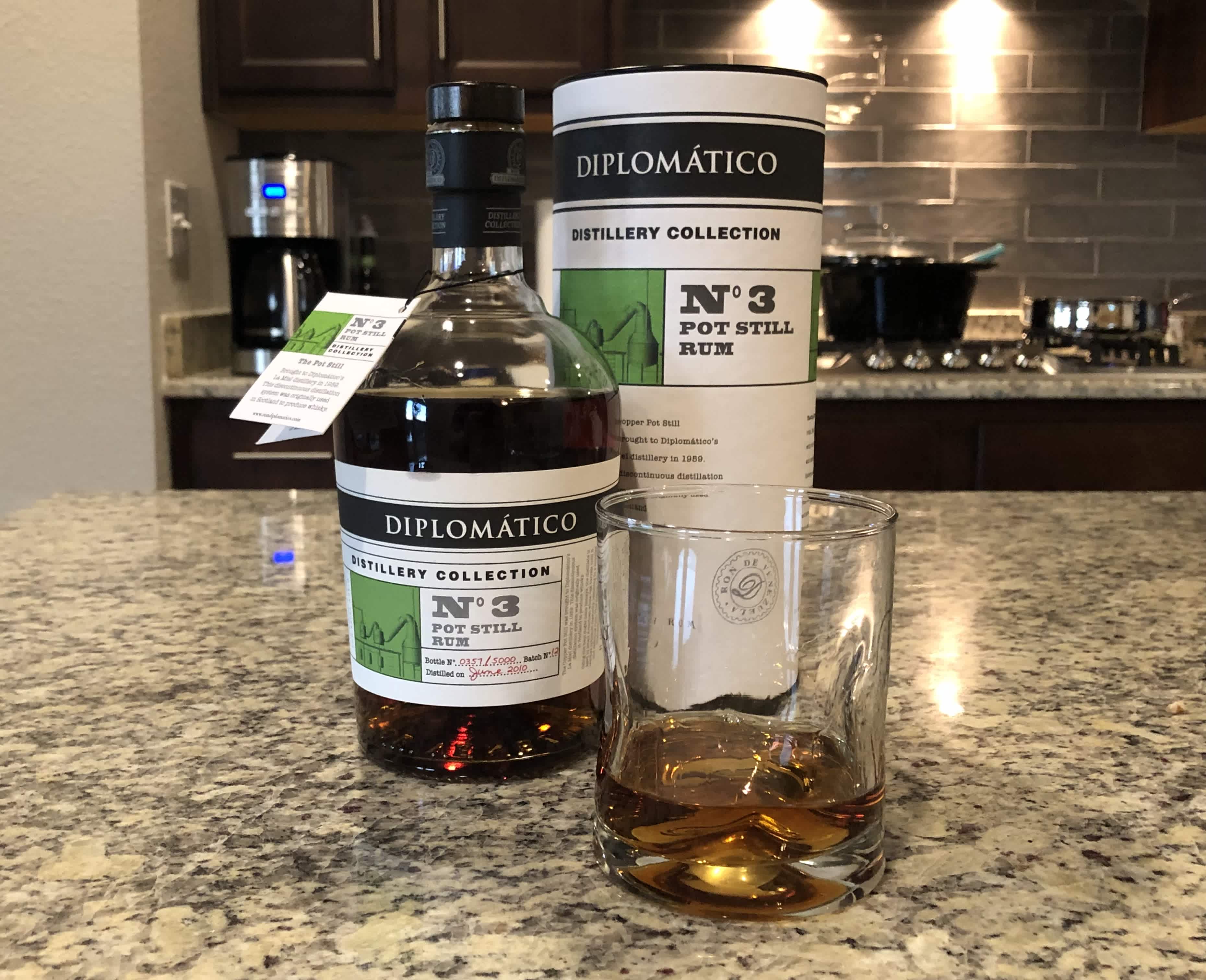 Diplomatico rum bottle and storage cylindar sitting on a kitchen counter next to a rocks glass filled with a few ounces of rum