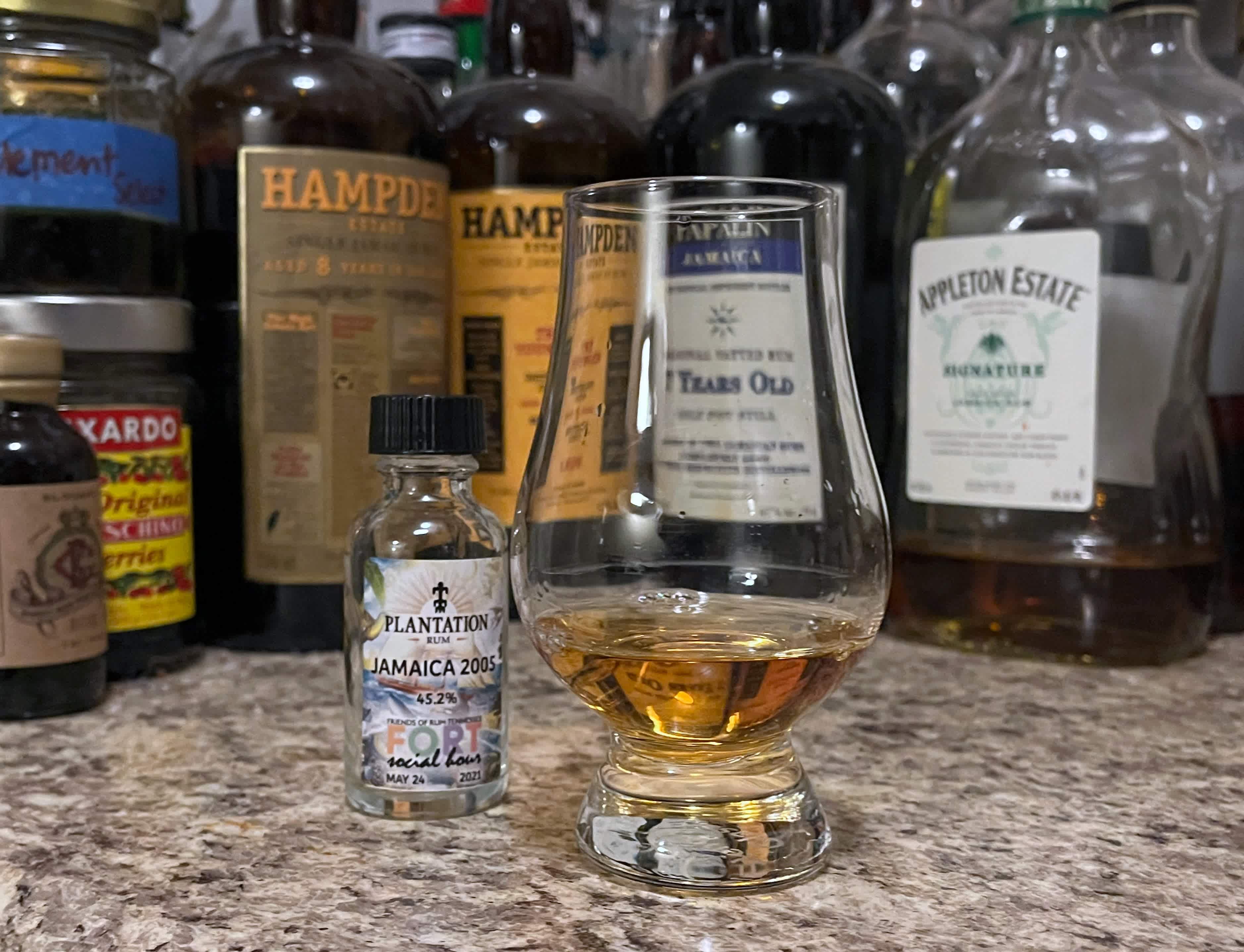 A sample bottle of Plantation Jamaica 2005 next to a glencairn of rum on a kitchen counter