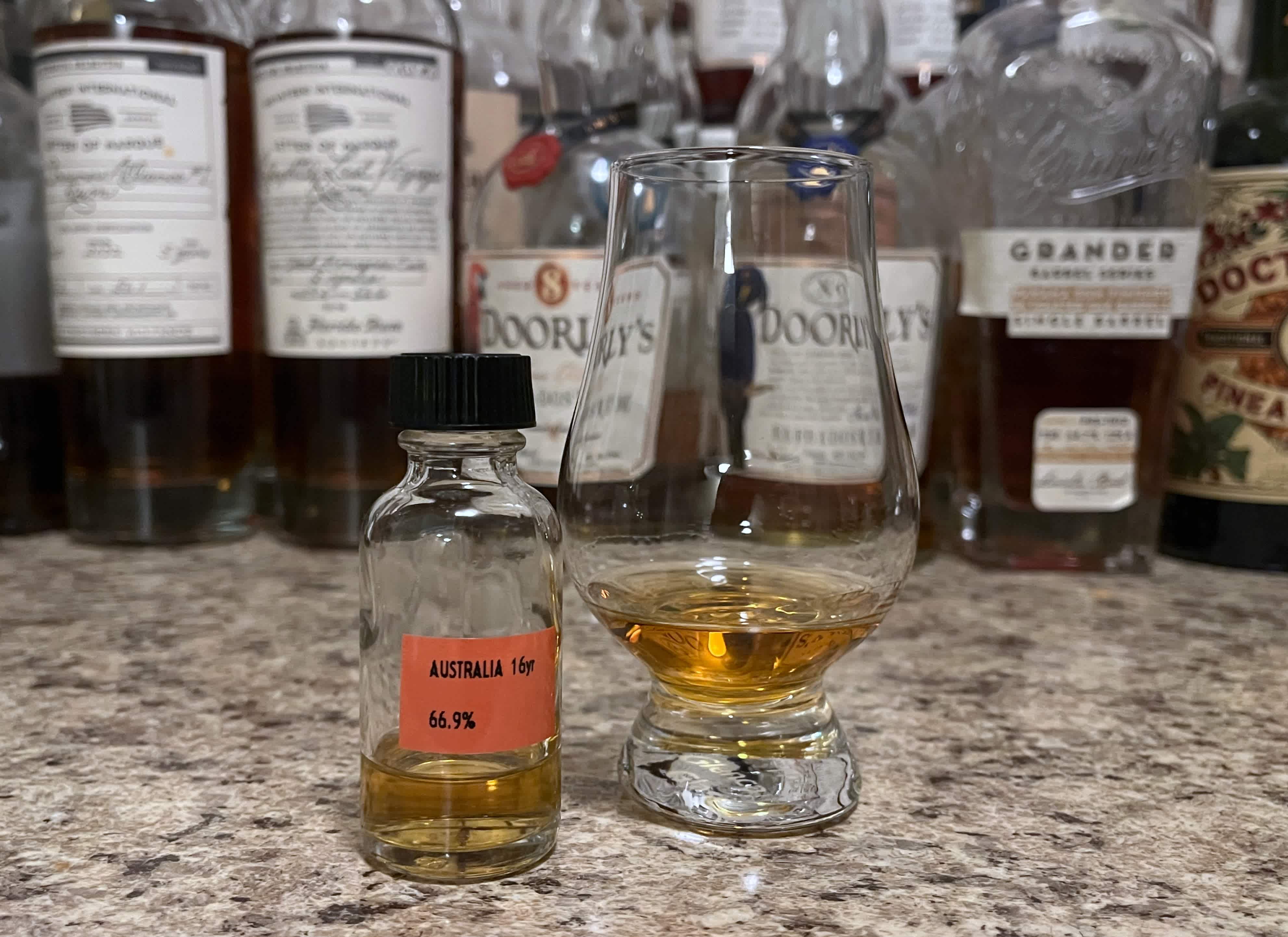 A sample bottle of Raising Glasses Australia next to a glencairn of rum on a kitchen counter