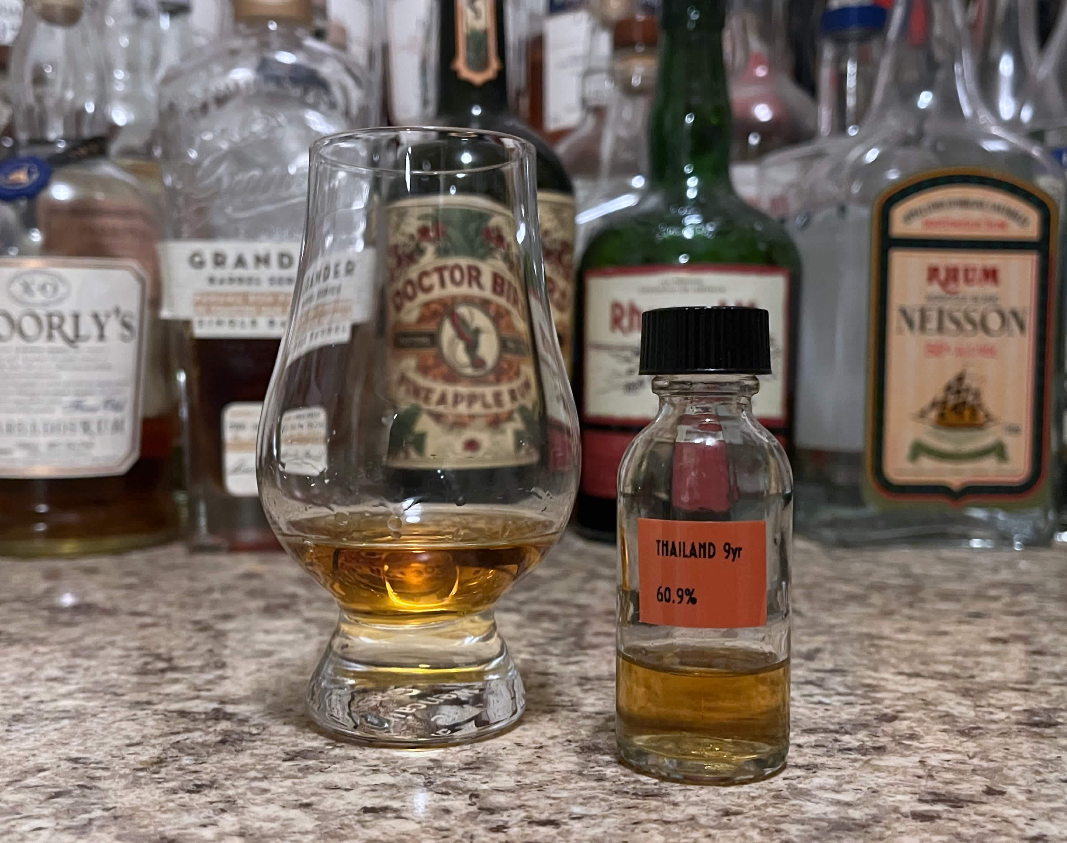 A sample bottle of Raising Glasses Thailand next to a glencairn of rum on a kitchen counter