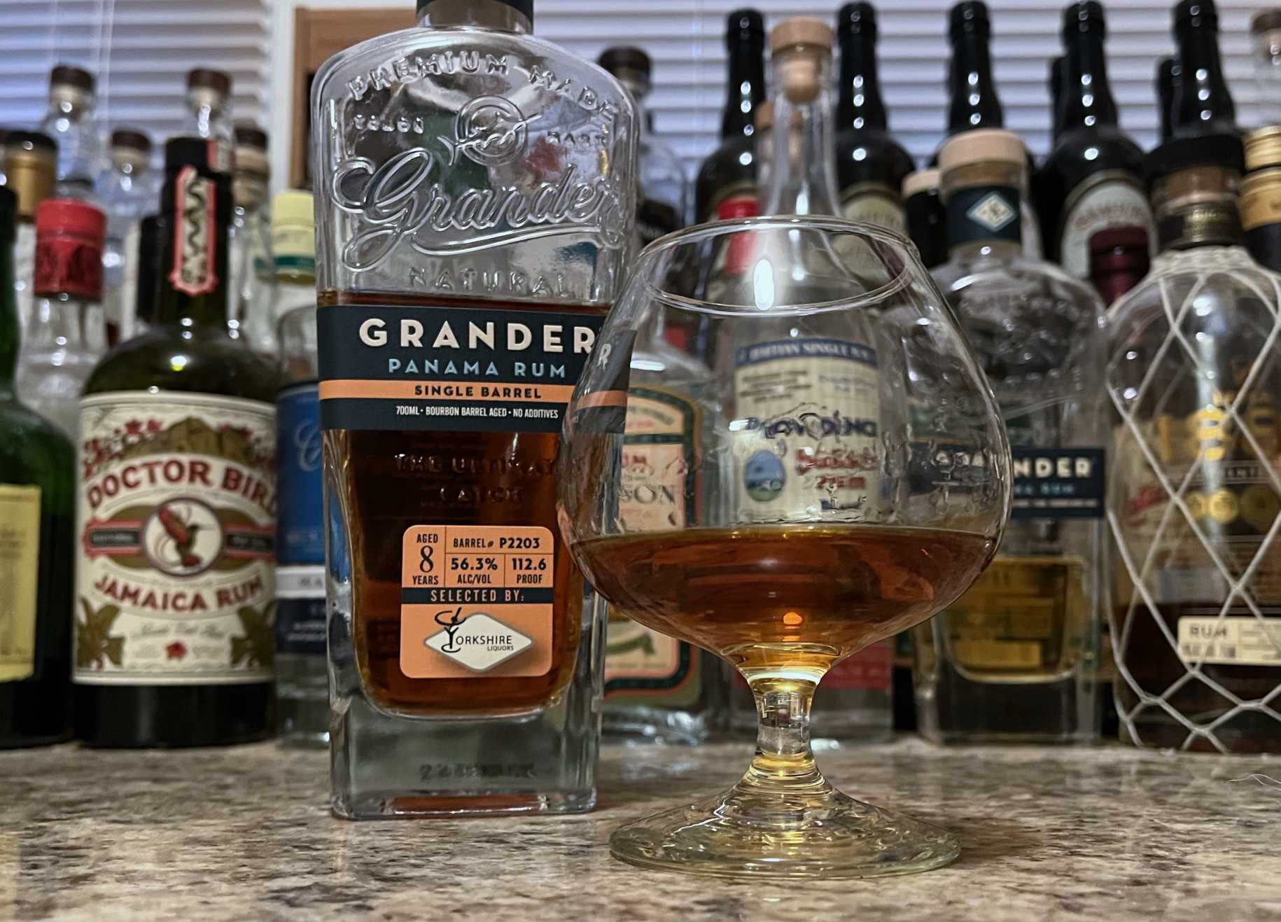 Bottle of Grander Single Barrel P2203 rum next to a snifter of rum on a countertop