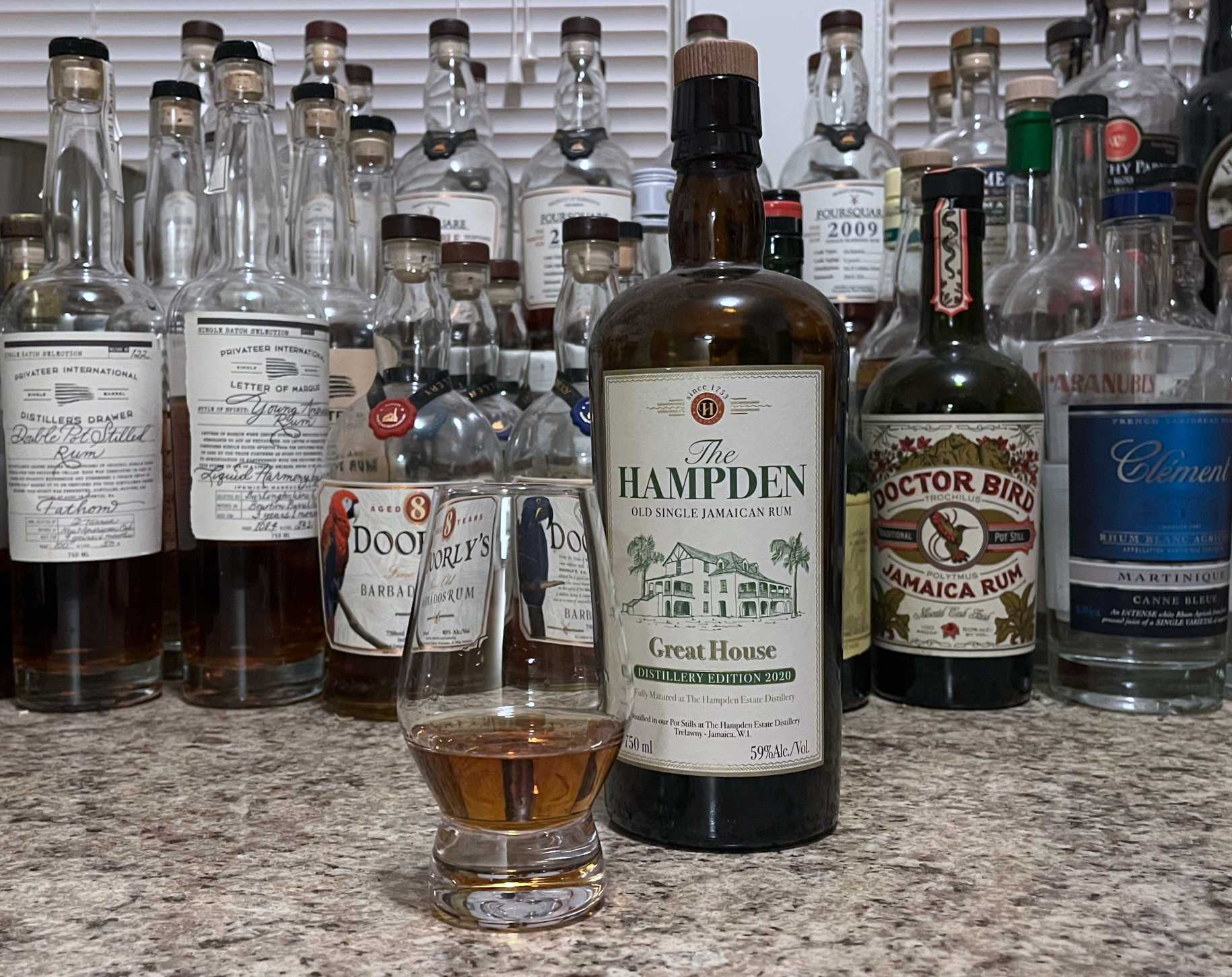 A bottle of Hampden Great House 2020 next to a glencairn of rum on a kitchen counter