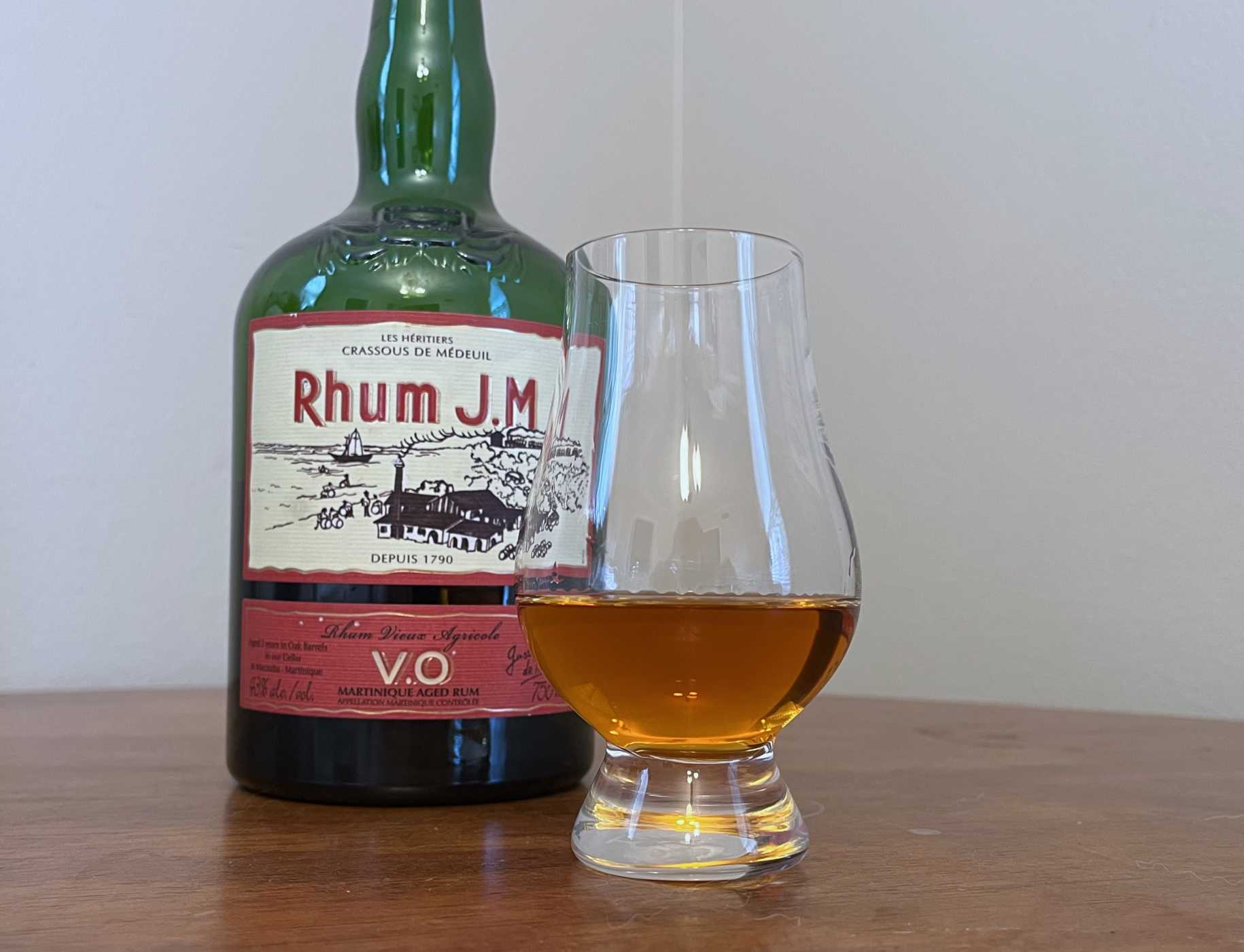 Bottle of Rhum JM VO next to a glencairn of rum on a table