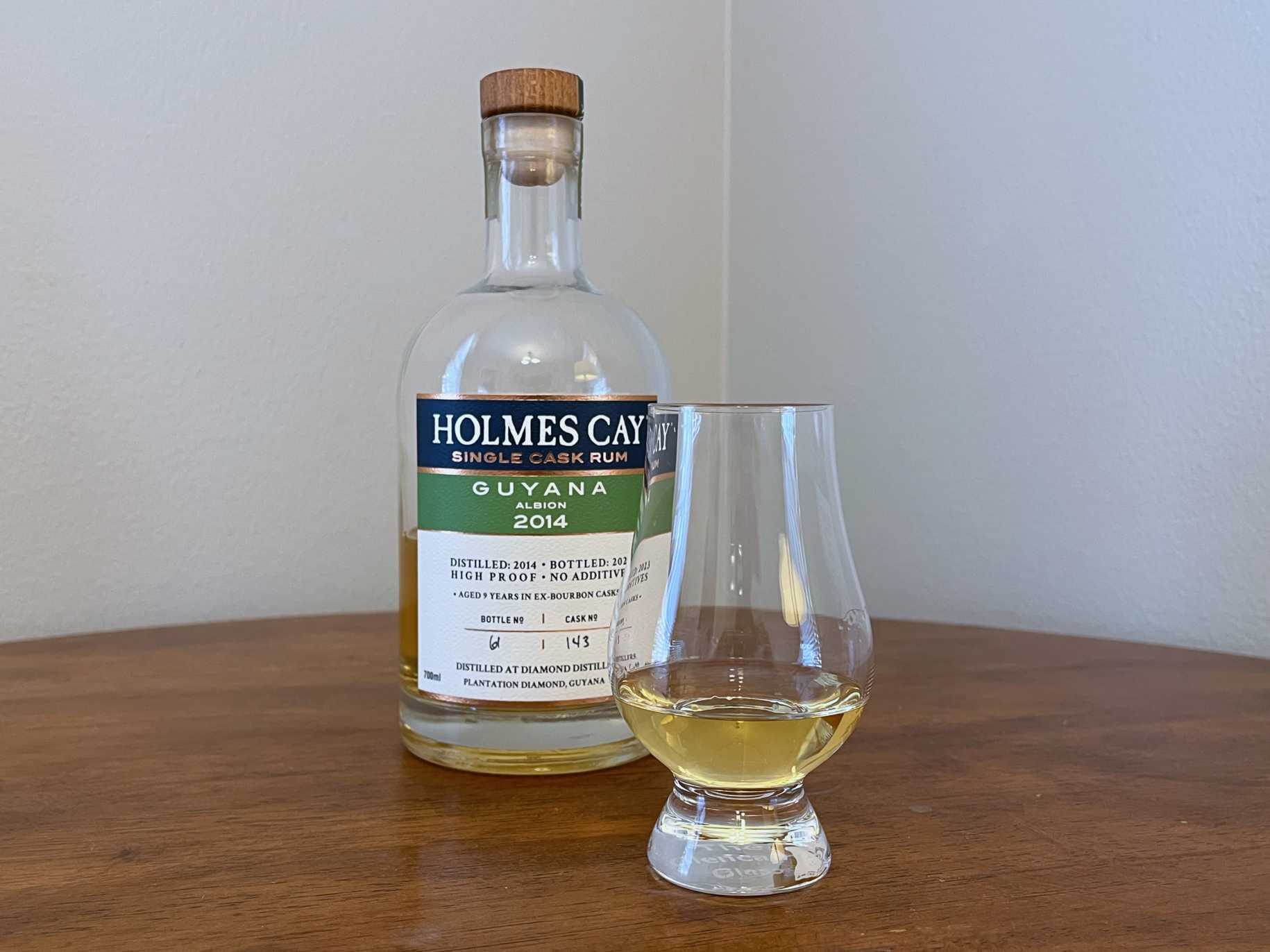 Bottle of Holmes Cay Guyana rum on a tabletop next to a Glencairn of rum