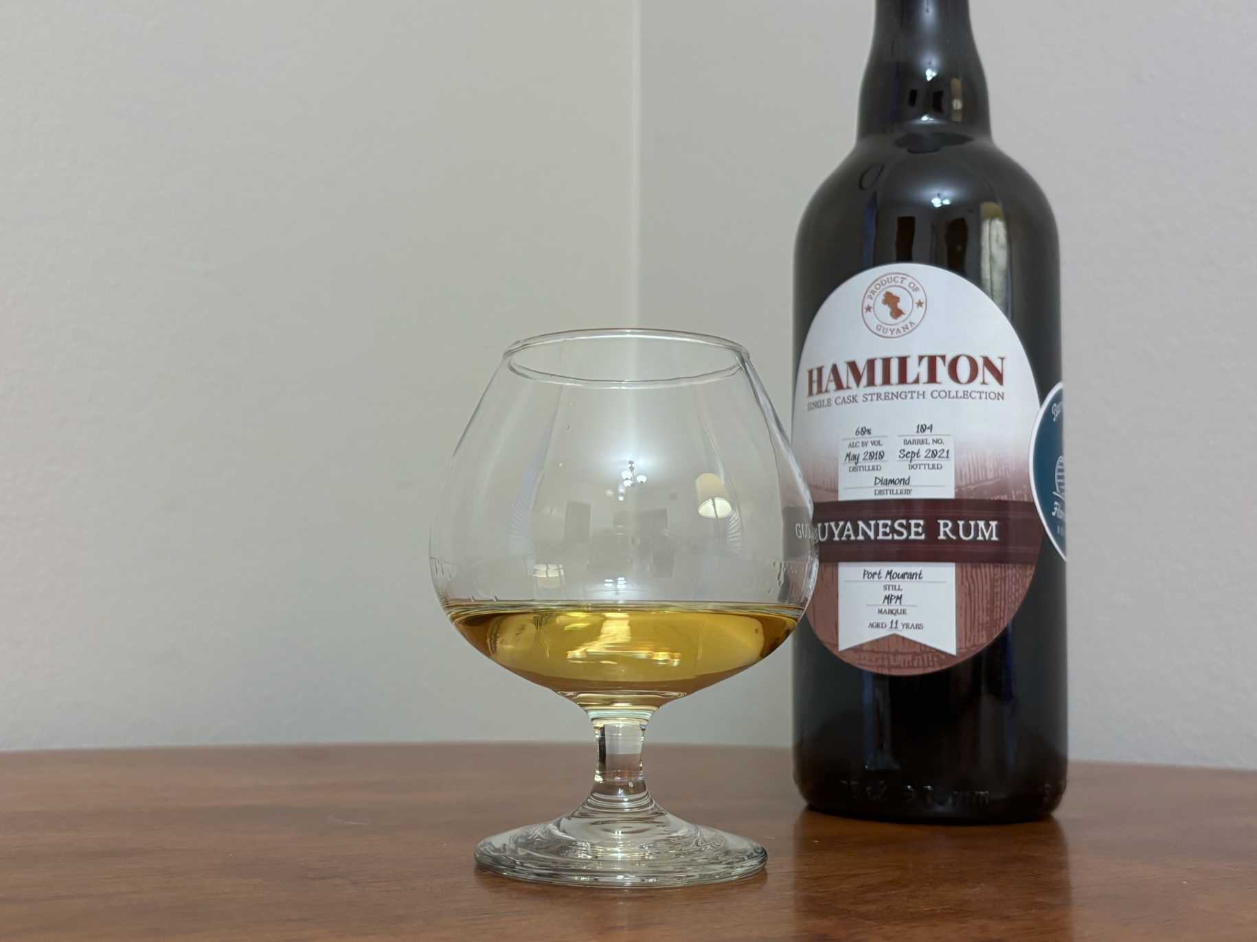 A bottle of Hamilton Single Cask Port Mourant next to a glass of rum