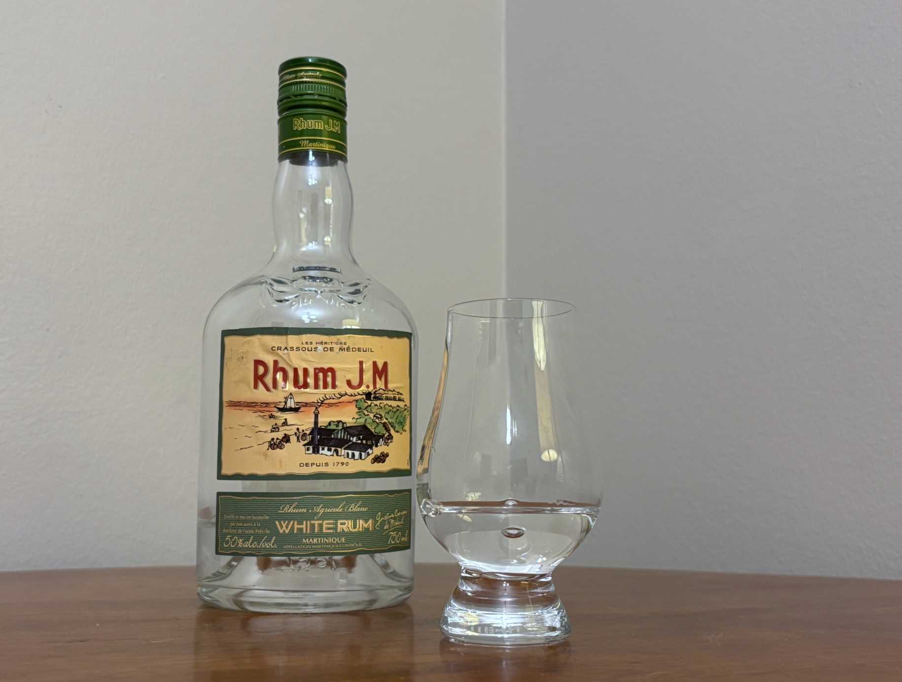 A bottle of Rhum JM Blanc 100 proof next to a glass of rum