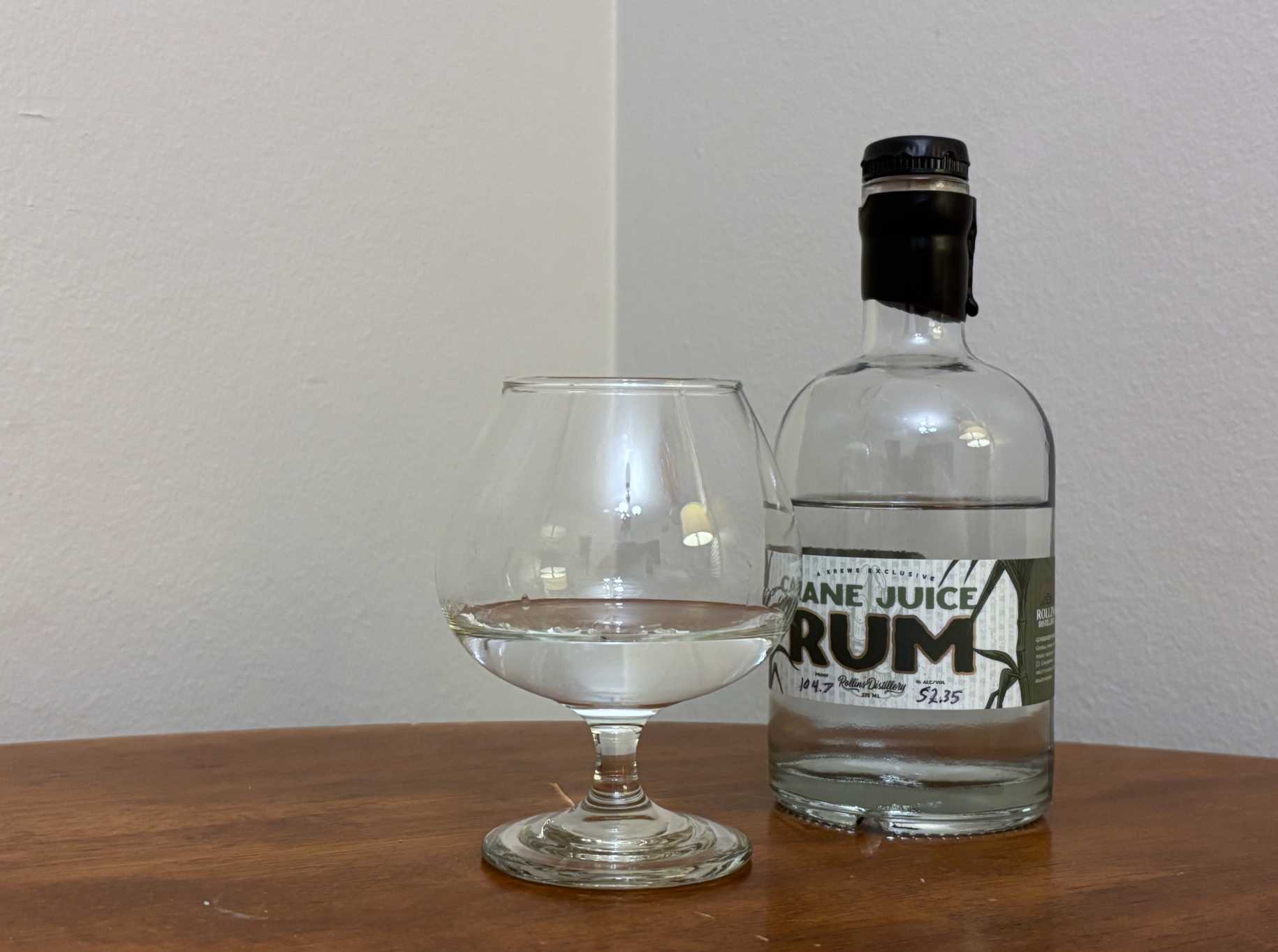 A bottle of Krewe Exclusive Cane Juice Rum next to a glass of rum