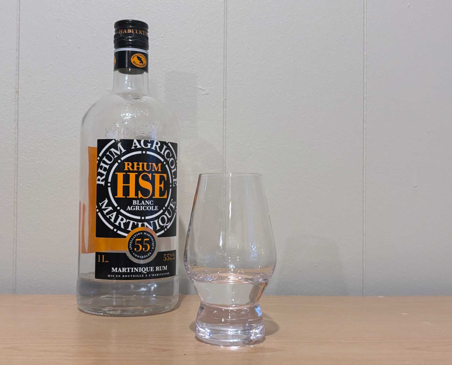 A bottle of Rhum HSE Blanc Agricole 55º next to a glass of rum