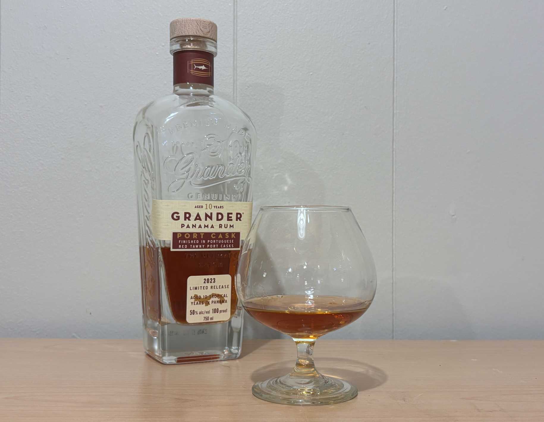 A bottle of Grander Port Cask Finish 10 year next to a glass of rum
