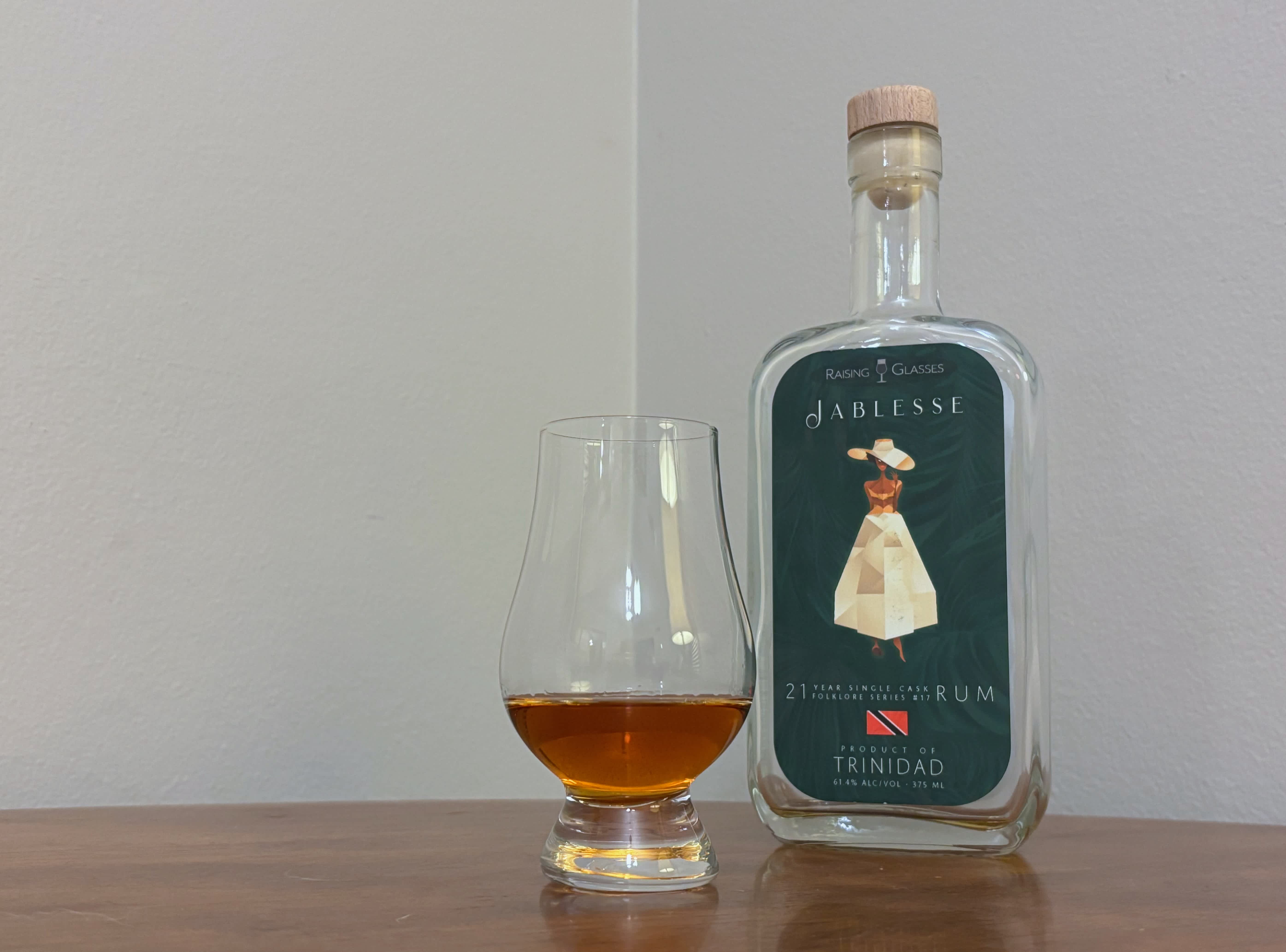 A bottle of Raising Glasses Jablesse Trinidad 21 year next to a glass of rum