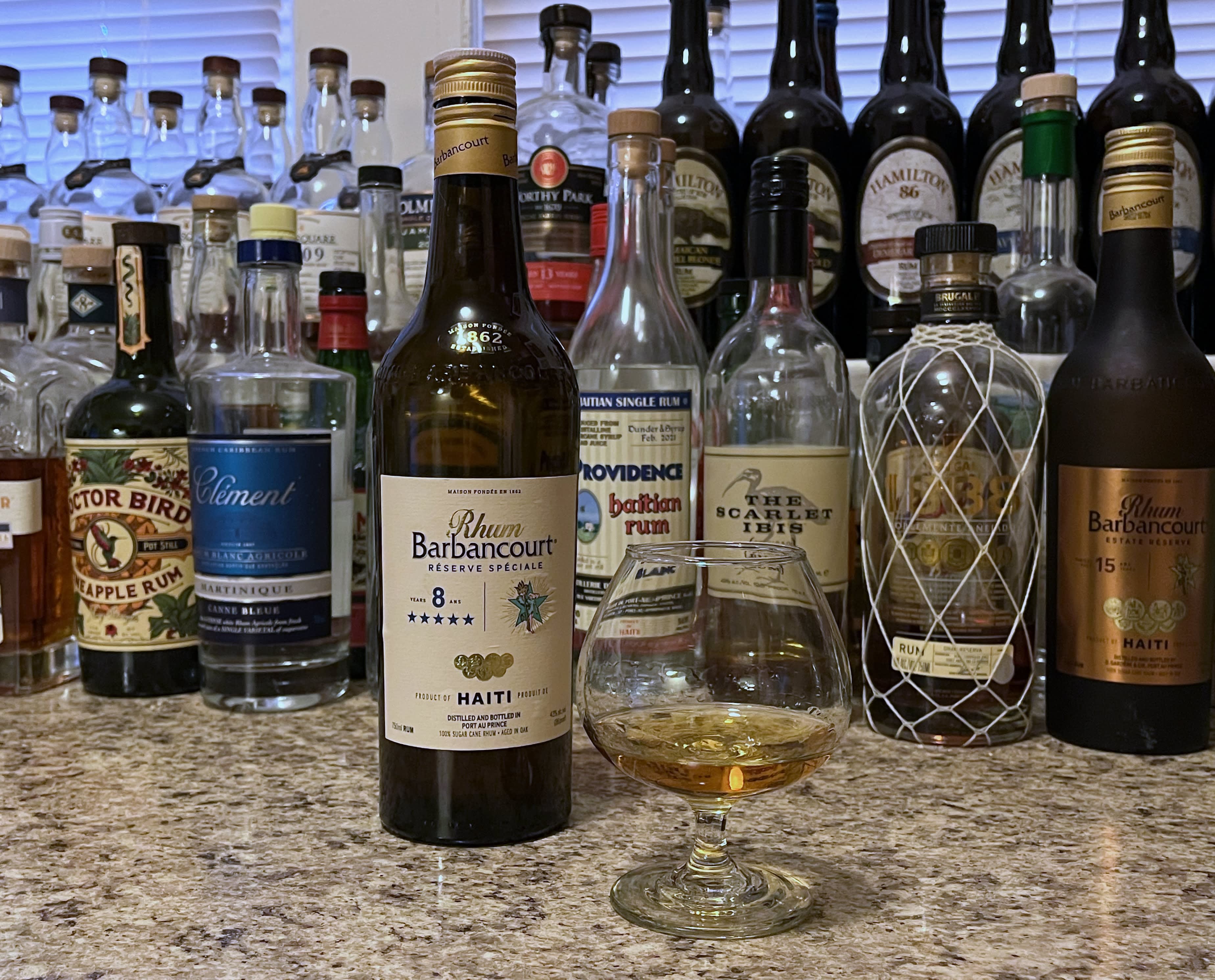 A bottle of Rhum Barbancourt 8 year next to a glencairn of rum on a kitchen counter