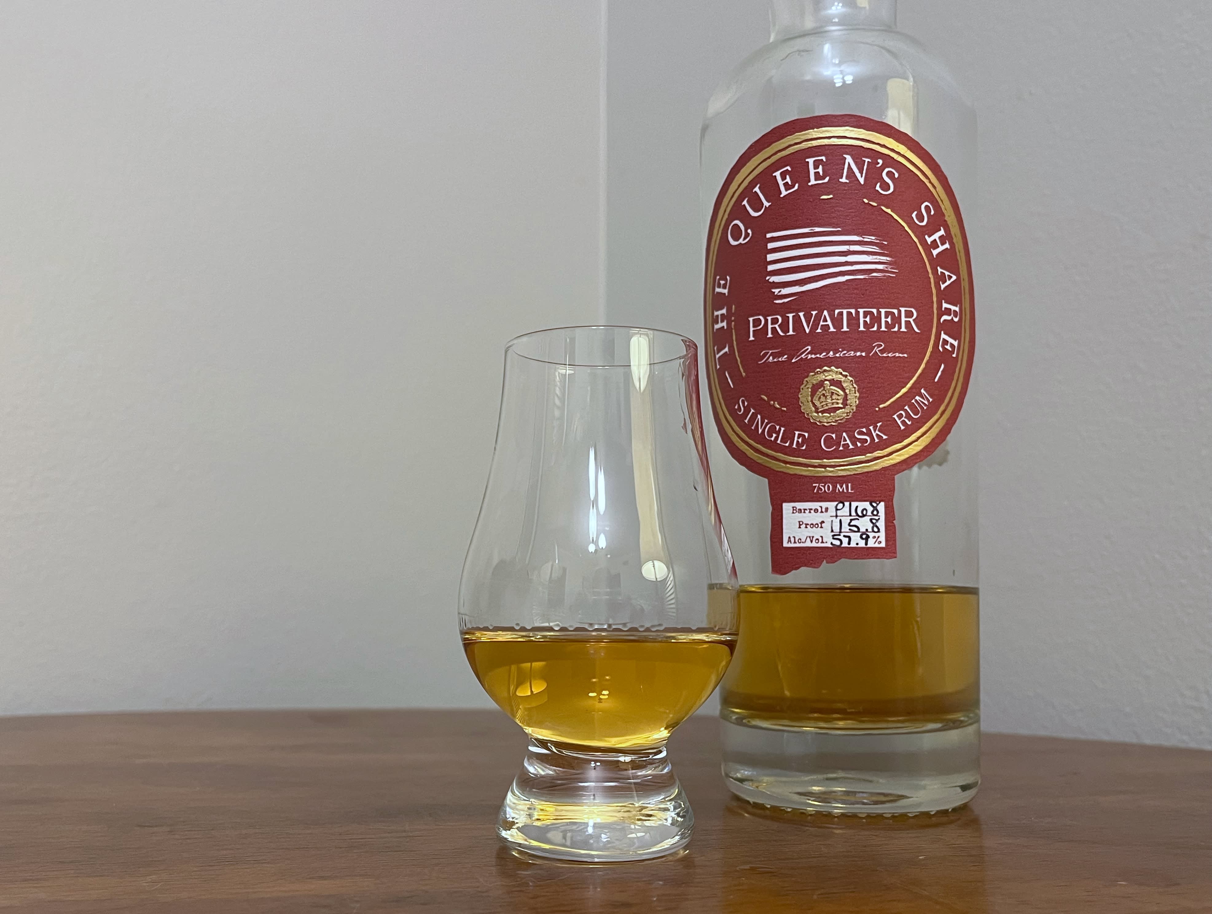 Privateer Queen's Share bottle sitting on a table next to a glass of rum