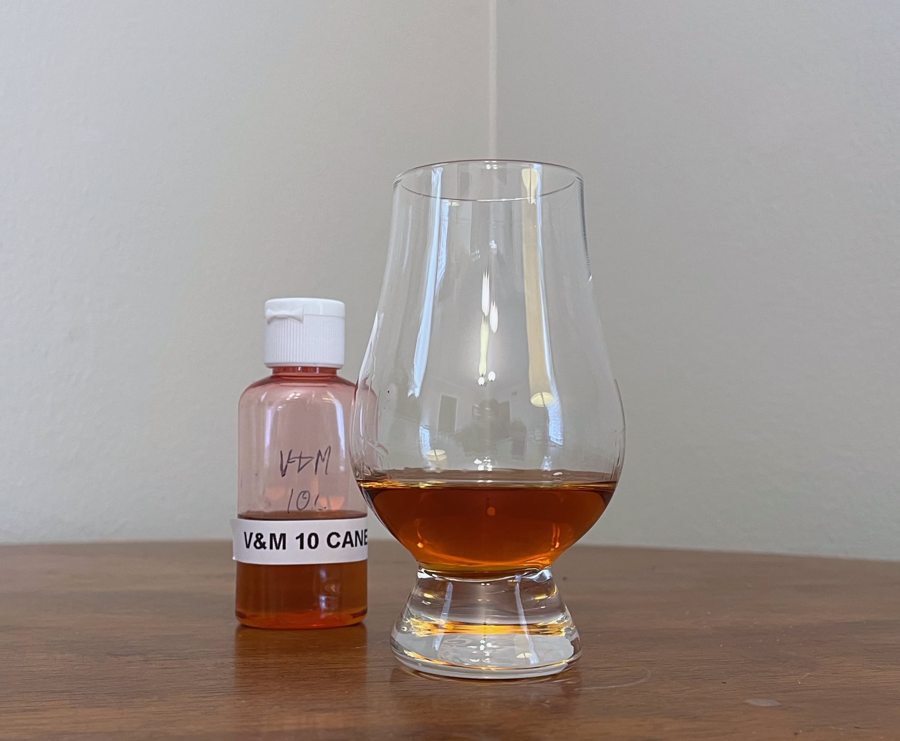 A sample bottle of Valinch & Mallet Ten Cane 2008 next to a glass of rum on a table