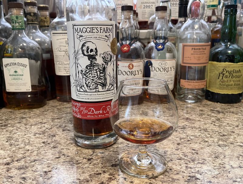 A bottle of Maggie's Farm 50/50 next to a glencairn of rum on a kitchen counter